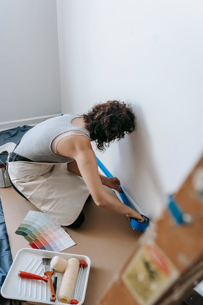 A woman applying adhesive tape to a wall for a renovation project indoors.